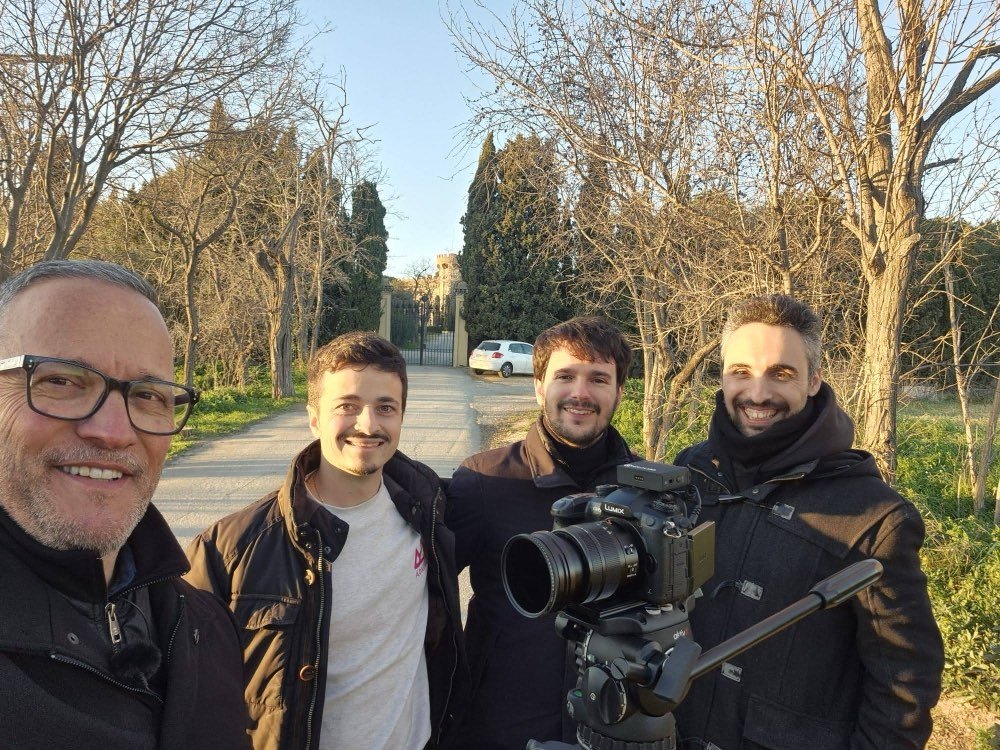 Cuatro personas del equipo, con la cámara al hombro, en un camino entre cipreses.