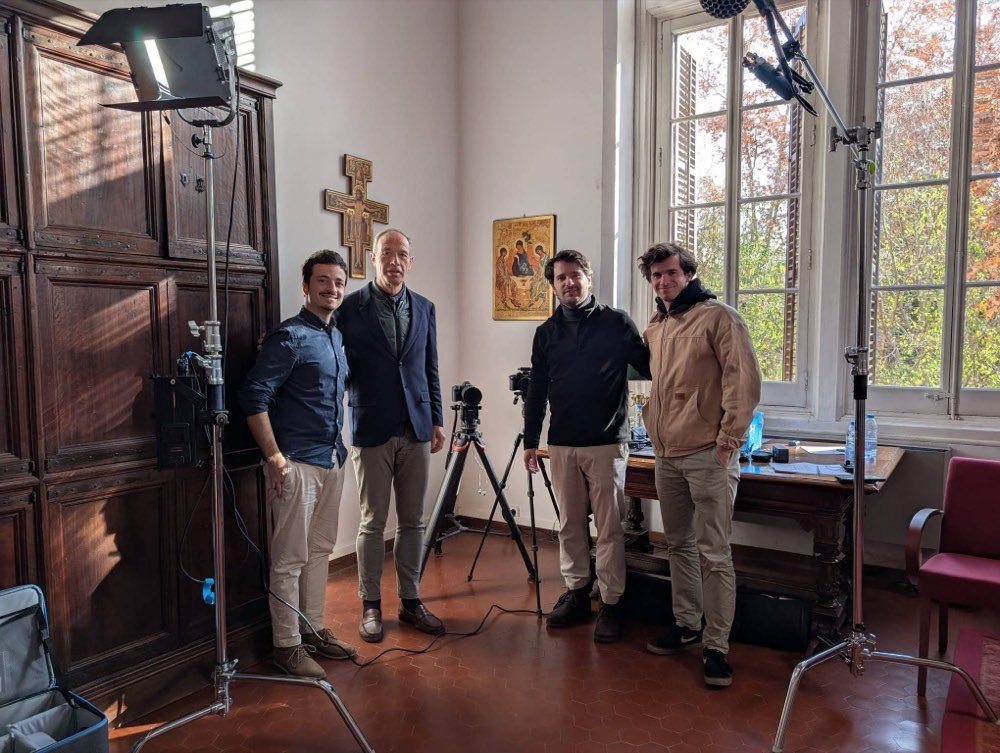 El equipo, junto a focos y cámara, en una sala con ventanales y un crucifijo en la pared.