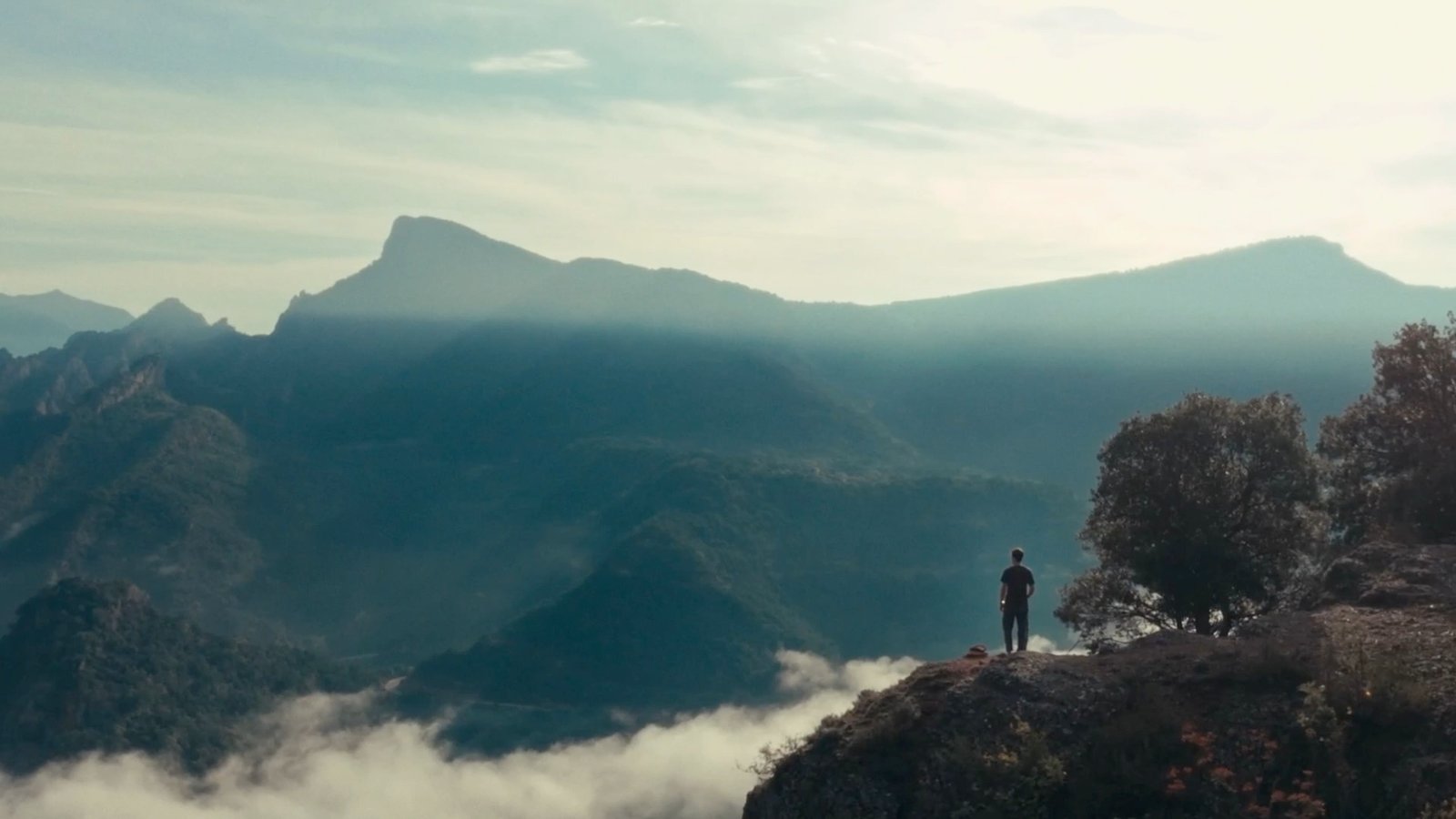 Un hombre contempla desde un risco un valle de montañas cubierto por un mar de nubes.