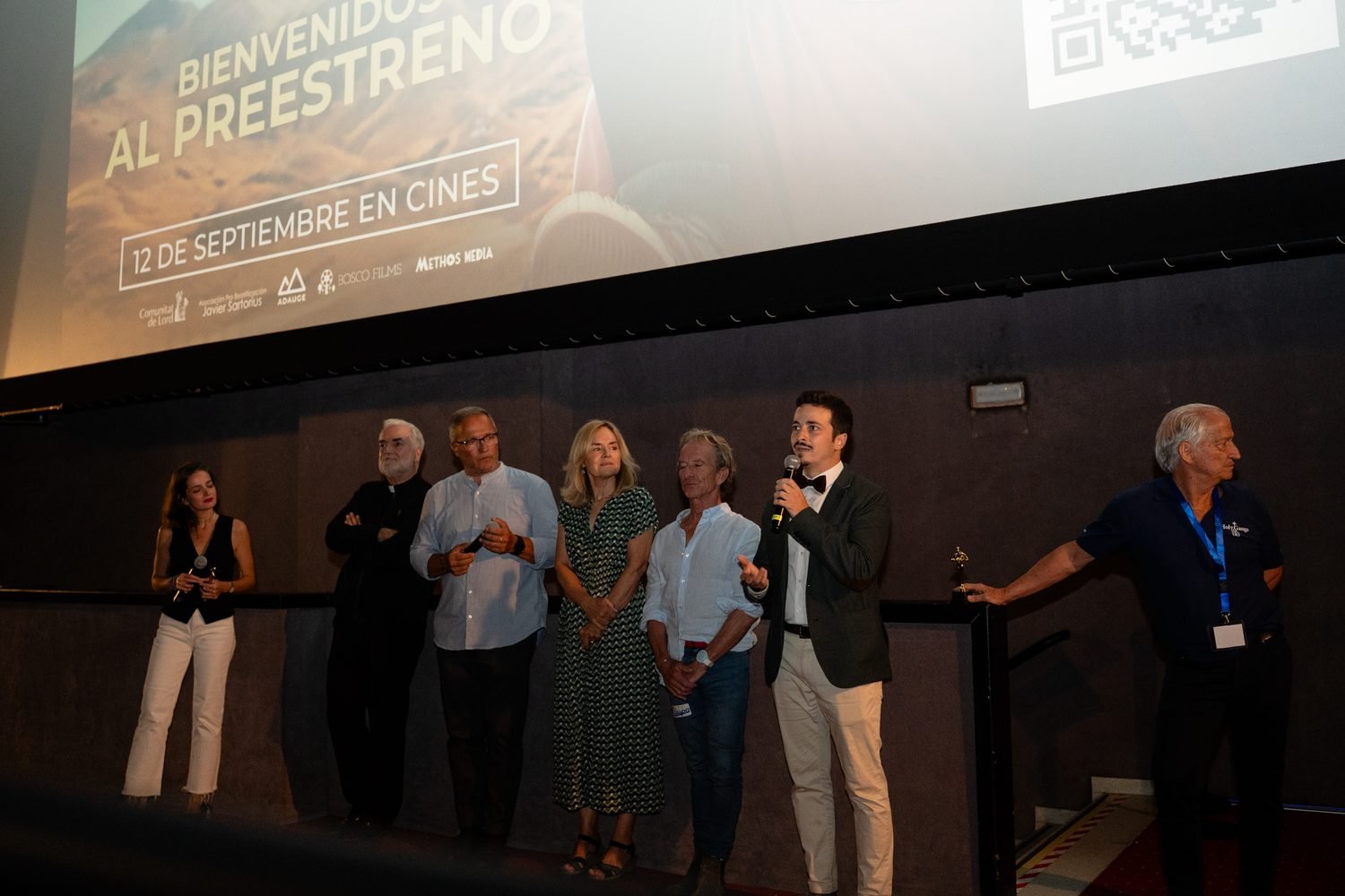 El equipo y varios invitados hablan al público desde la tarima de un cine, bajo la pantalla del preestreno.