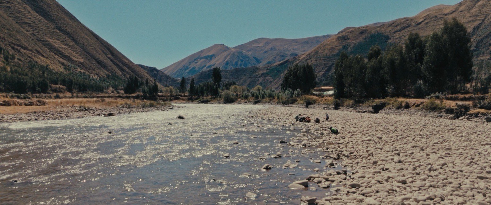Un río poco profundo entre montañas y árboles.