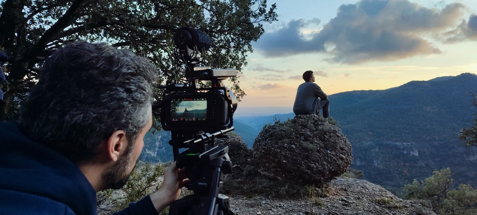Rodaje de Solo Javier: un cámara filma a un joven sentado sobre una roca frente a las montañas al atardecer.